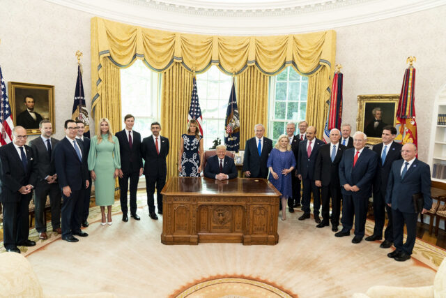 President Trump seated at the Resolute Desk with Israeli, Emirati and Bahraini leaders and U.S. officials standing in the Oval Office